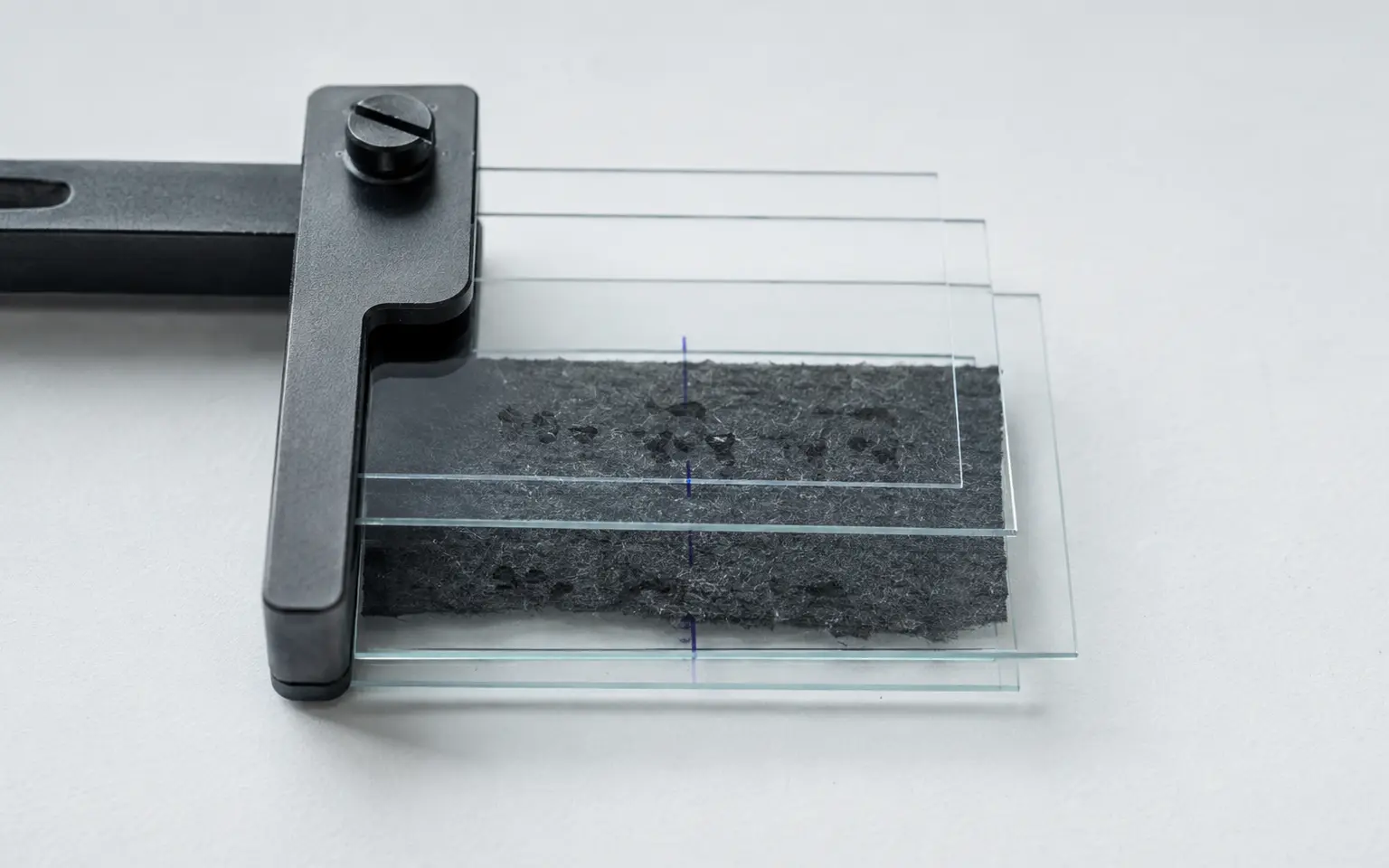 Layered calibration plates holding a dark fibrous sample under cold light